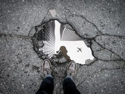 person staring at their reflection in a watery pothole