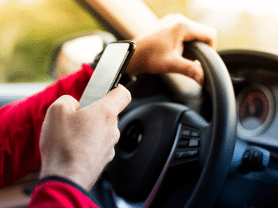 Close-up of a driver holding a smartphone while steering a car, illustrating distracted driving in Santa Barbara and the evidence used to prove phone use after a crash.