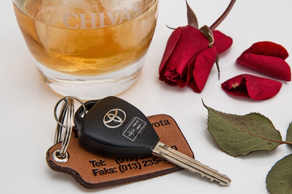 car key laying next to alcohol and a rose