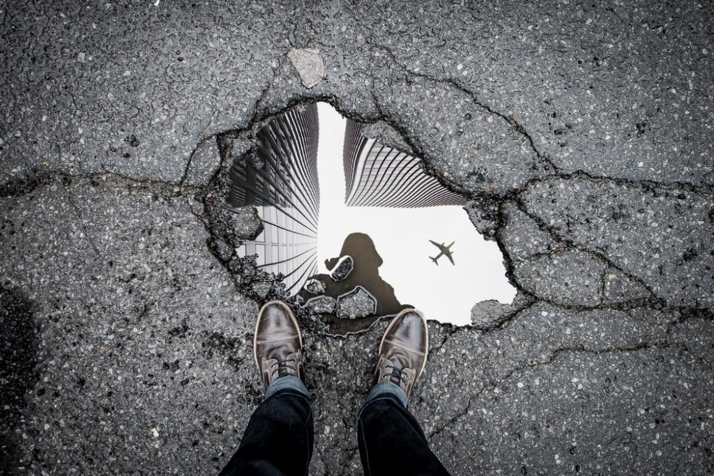 person staring at their reflection in a watery pothole